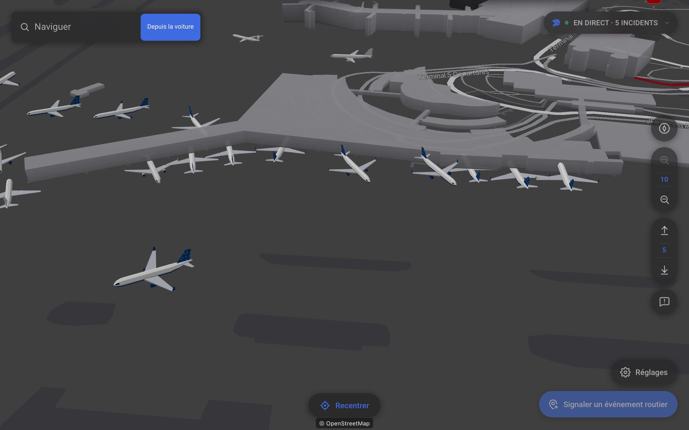 Une carte 3D inclinée, de nuit, du terminal 5 de JFK : des avions JetBlue aux dérives bleues stationnés face au terminal, un autre avion JetBlue qui roule au premier plan, et d’autres appareils sur les voies de circulation au-delà.